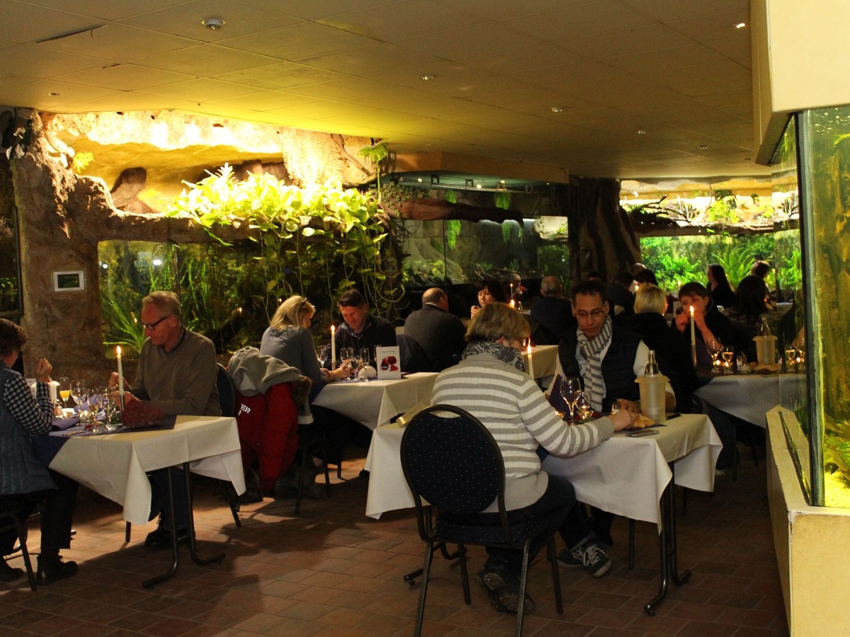Menschen essen vor gedeckten Tischen in einem Durchgang zwischen den Aquarien.