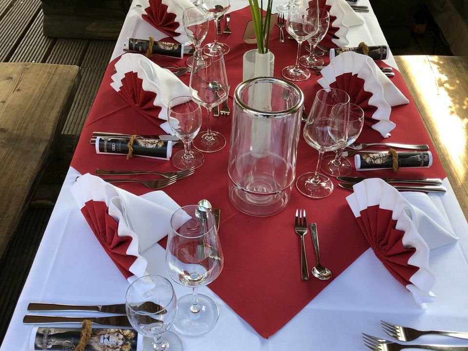 Festlich gedeckter Tisch mit weißen und roten Servietten, Blumen und gläsernem Windlicht.