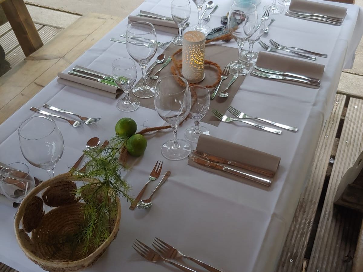 Gedeckter Tisch mit weißer Tischdecke, Besteck, Gläsern, Kerze und Deko mit Limetten.