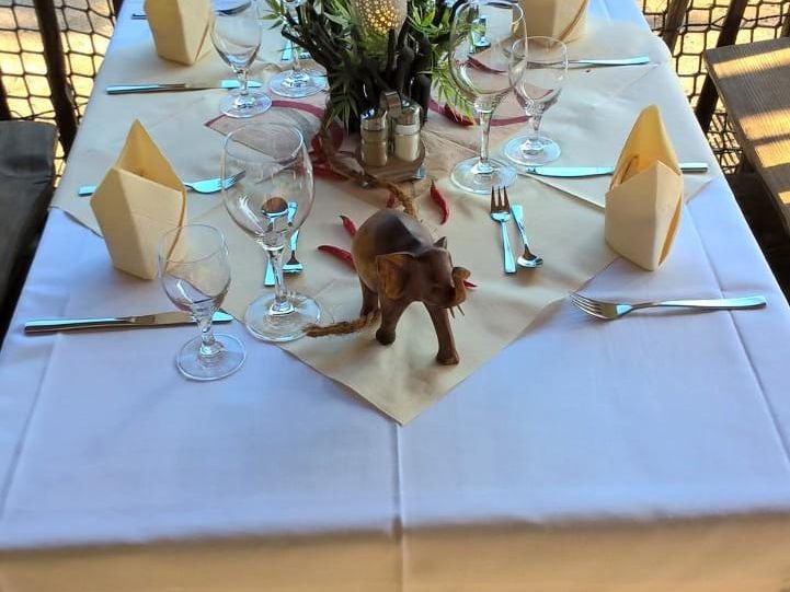 Gedeckter Tisch mit weißer Tischdecke, gefalteten Servietten, Glasflasche und Holz-Glücksbringer.