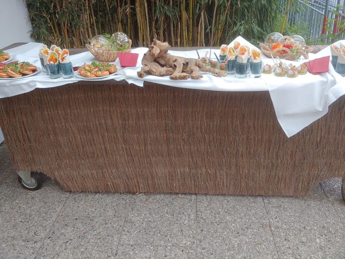 Buffettisch mit weißer Tischdecke und dekorativen Häppchen, davor Verkleidung aus Strohmatten, im Außenbereich.