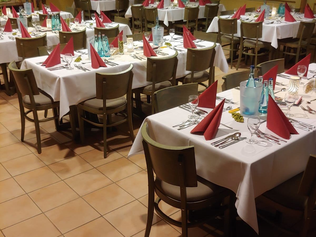 Festlich gedeckte Tische mit weißen Tischdecken und roten Servietten in einem Restaurant mit Holzmöbeln.