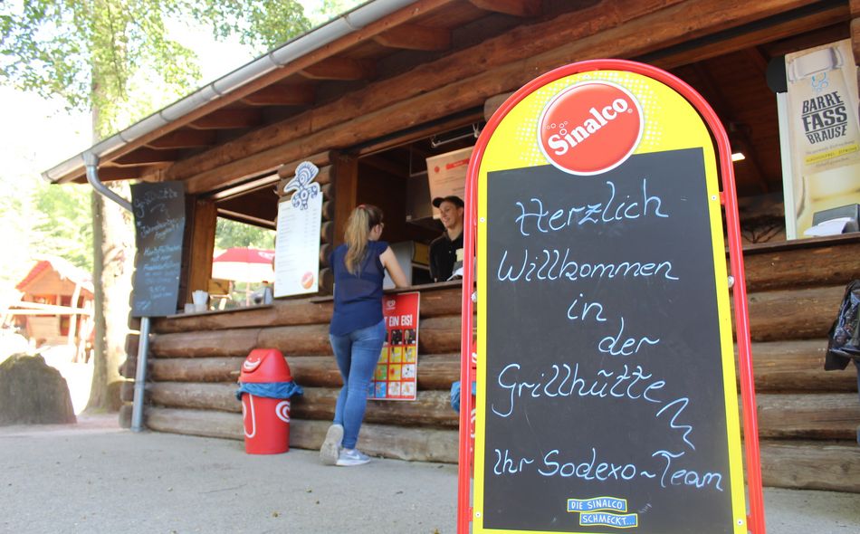 Holzhütte mit offenem Verkaufstresen und einem großen Willkommensschild davor.