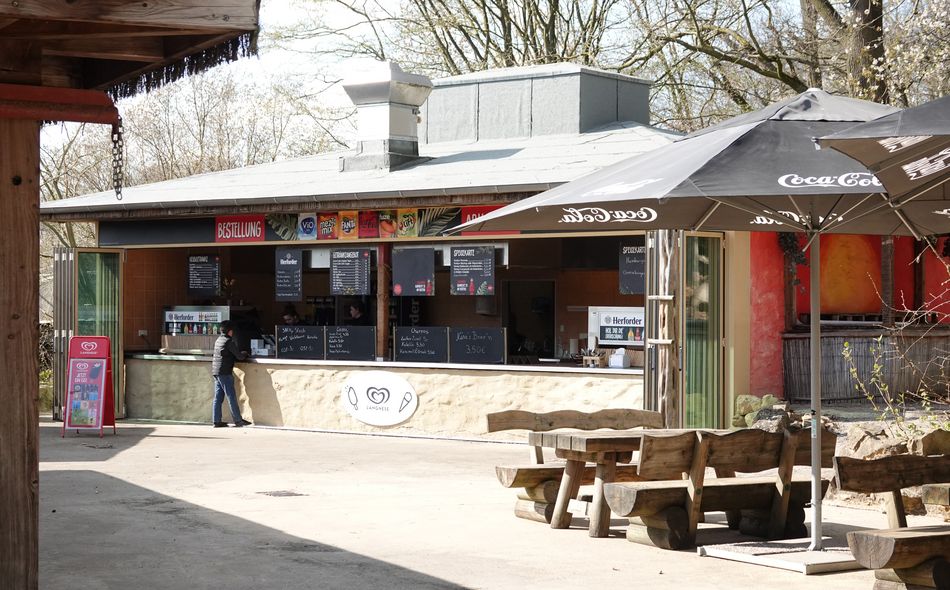 Verkaufsstand mit Außentresen, Holzbänken und Coca-Cola-Schirmen im Frühling.