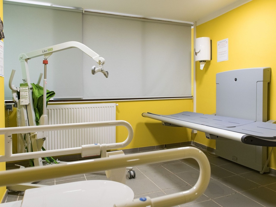 Barrierefreier, gelb gestrichener Pflegeraum mit Liftersystem und Liege.