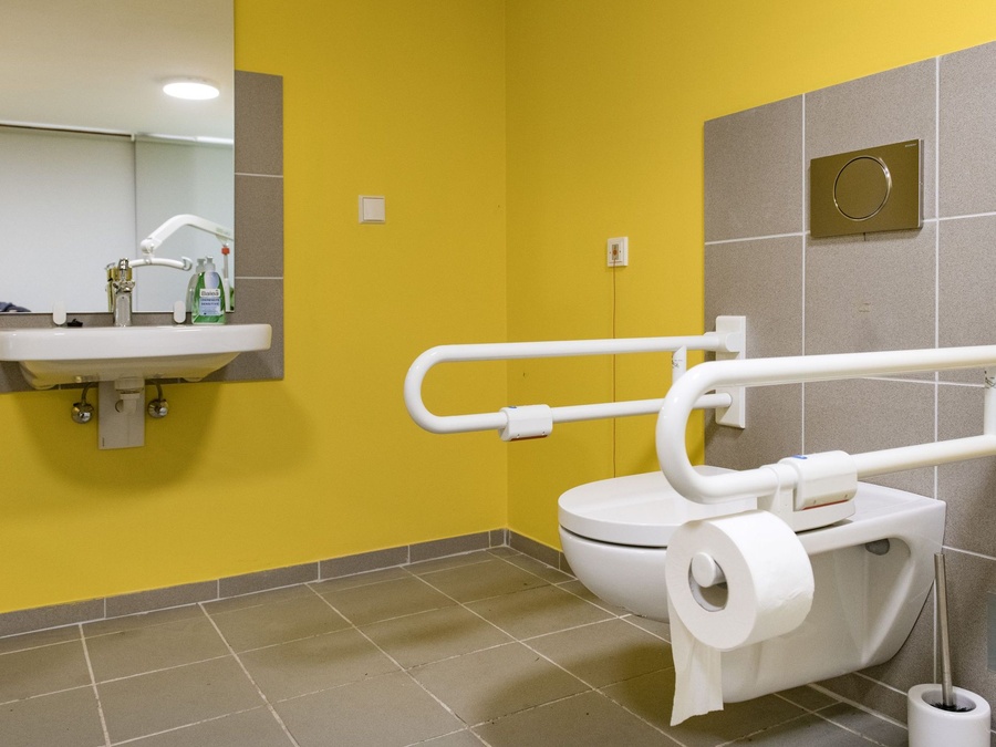Barrierefreies WC mit Haltegriffen, Waschbecken mit Spiegel und gelber Wand.